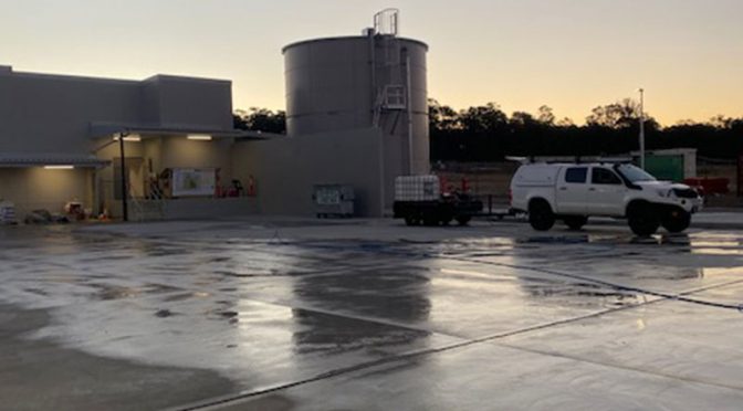 Early morning shot of an industrial water treatment facility with storage tanks, reflecting the calm start of the day on its wet concrete grounds.