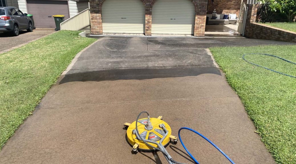 A clear before and after comparison of a driveway cleaning, with a pressure washer tool in the foreground and the clean path highlighted against the still-dirty surface.