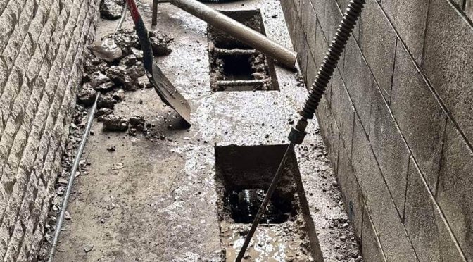 Close-up image of foundation underpinning work in progress, featuring excavated square pits and steel rebar for structural reinforcement, a crucial step in building stability and repair.