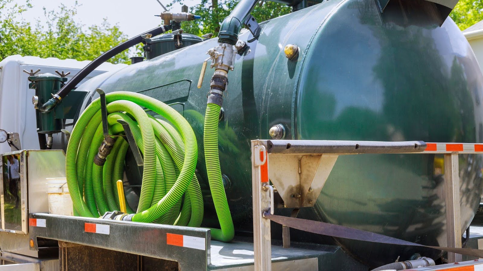 Detailed view of a vacuum truck's storage tank and green suction hoses, showcasing the specialised equipment used for industrial and municipal cleaning services.