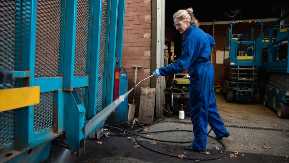 Commercial power washing expert in protective gear thoroughly cleans industrial machinery, ensuring high cleanliness standards for the facility.