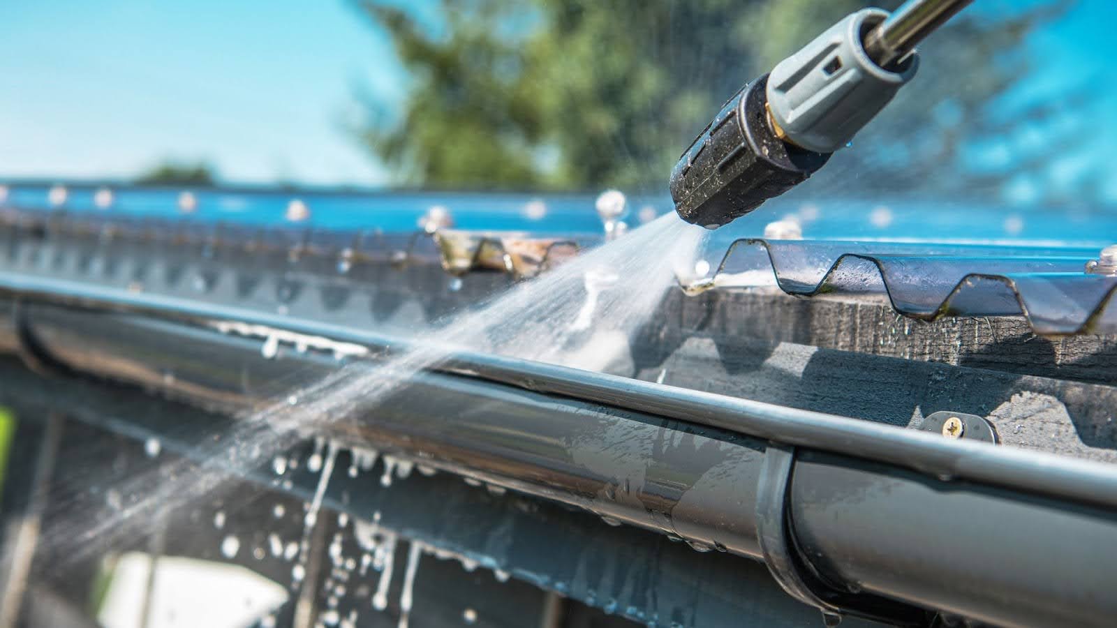 Close-up of a gutter cleaning service professional using a high-pressure washer to clear debris from a rain gutter, ensuring proper drainage and home maintenance. 