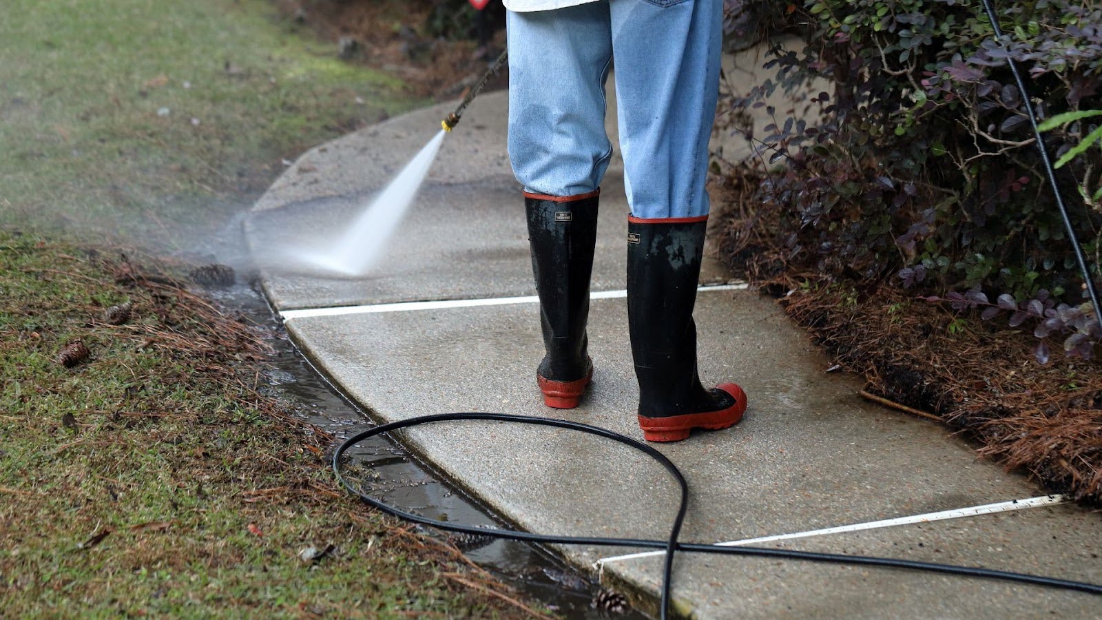 Close-up of pressure cleaning in progress, with a powerful spray cleaning a concrete walkway.