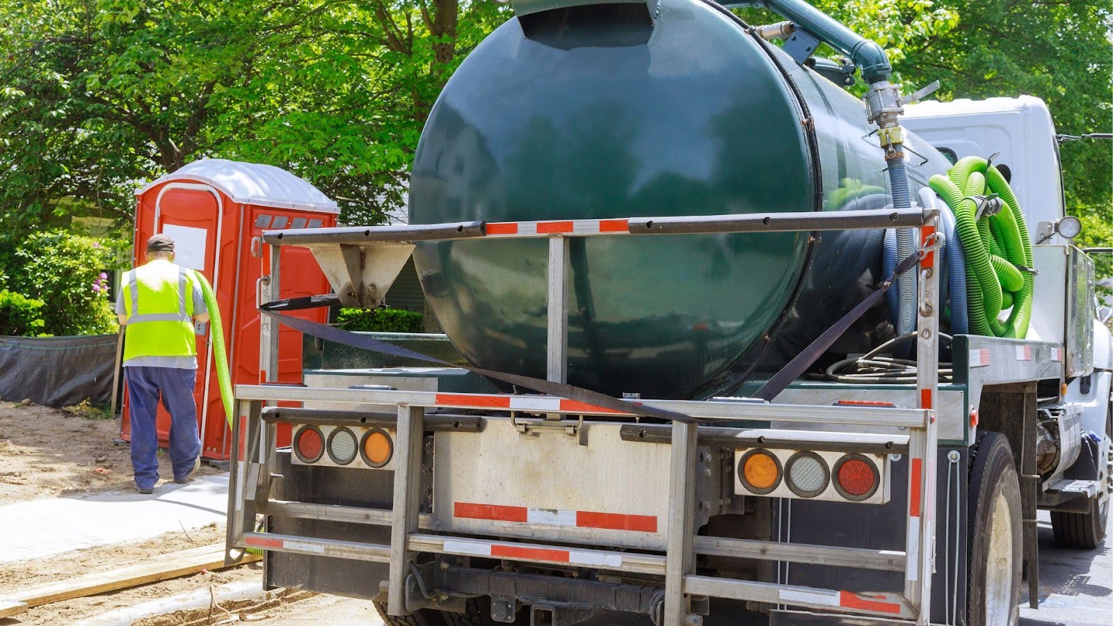 Vacuum truck parked at a construction site with a worker in visibility gear nearby, highlighting the truck's large tank and green suction hoses for waste management.