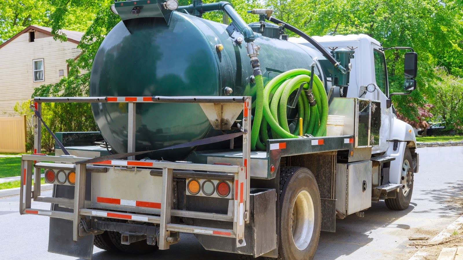 A vacuum truck equipped with hoses and a large storage tank parked on a residential street, ready for cleaning and waste removal services.